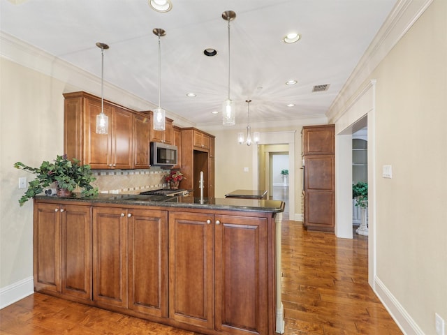 kitchen with brown cabinets, stainless steel microwave, backsplash, wood finished floors, and a peninsula