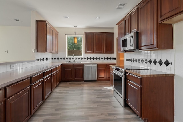 kitchen with light wood-style flooring, appliances with stainless steel finishes, decorative light fixtures, a sink, and backsplash