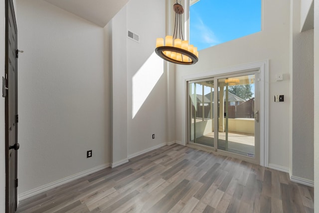 empty room featuring visible vents, a towering ceiling, an inviting chandelier, wood finished floors, and baseboards