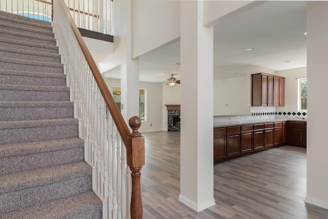 staircase featuring a ceiling fan, a fireplace, baseboards, and wood finished floors