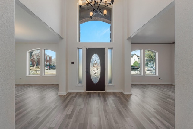 foyer entrance featuring wood finished floors, a towering ceiling, baseboards, an inviting chandelier, and crown molding