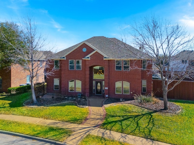 view of front of house with a shingled roof, a front yard, brick siding, and fence