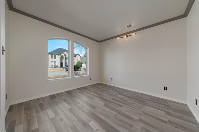 spare room featuring baseboards, visible vents, crown molding, and wood finished floors