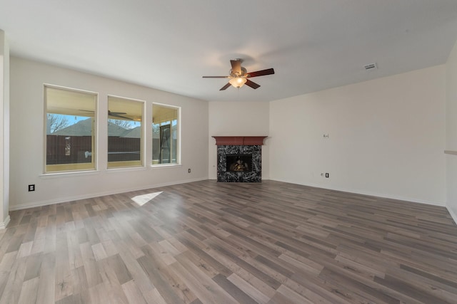 unfurnished living room featuring visible vents, a premium fireplace, ceiling fan, wood finished floors, and baseboards