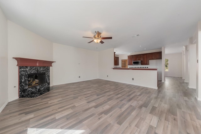 unfurnished living room with visible vents, light wood finished floors, a high end fireplace, and a ceiling fan