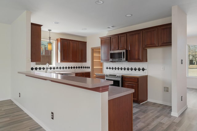 kitchen featuring pendant lighting, light wood finished floors, stainless steel appliances, visible vents, and a peninsula