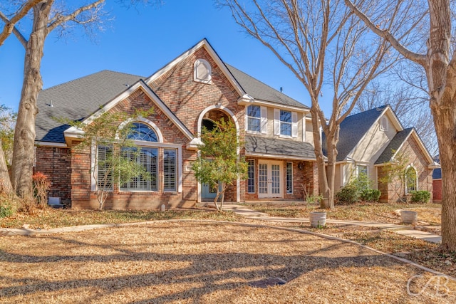 traditional home featuring french doors, brick siding, and roof with shingles