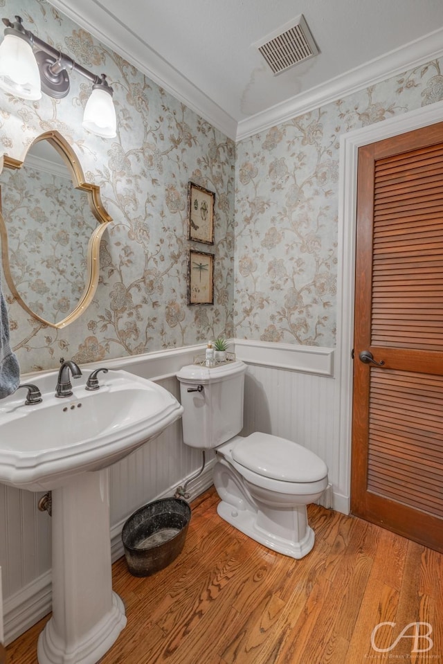 half bath with a wainscoted wall, visible vents, toilet, wood finished floors, and wallpapered walls