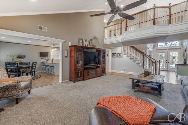 carpeted living room featuring visible vents, stairway, a high ceiling, crown molding, and french doors