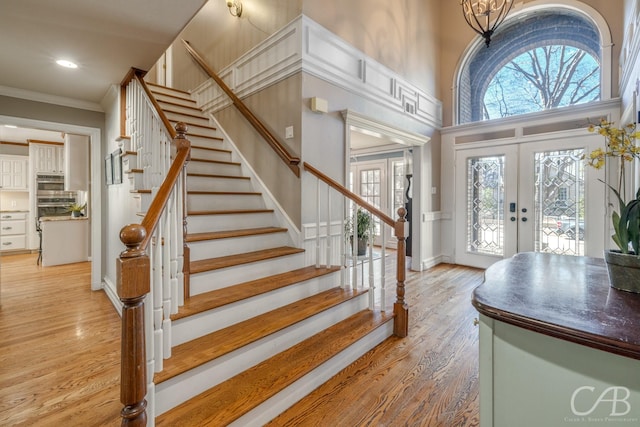 entrance foyer with stairway, a high ceiling, crown molding, french doors, and light wood-style floors