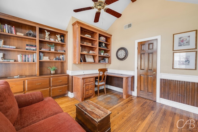 home office with light wood finished floors, visible vents, a ceiling fan, wainscoting, and built in desk