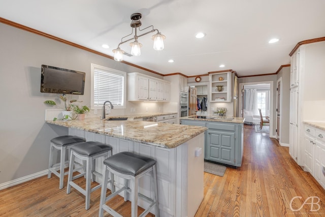 kitchen featuring a peninsula, light wood-type flooring, a sink, and a healthy amount of sunlight