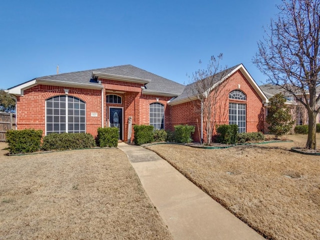 ranch-style home with brick siding, fence, and roof with shingles