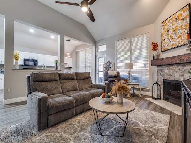 living area featuring lofted ceiling, baseboards, wood finished floors, and a stone fireplace