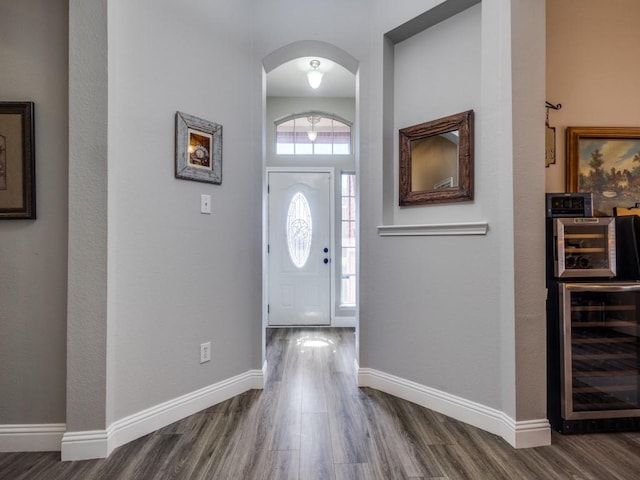 foyer featuring wine cooler, arched walkways, baseboards, and wood finished floors