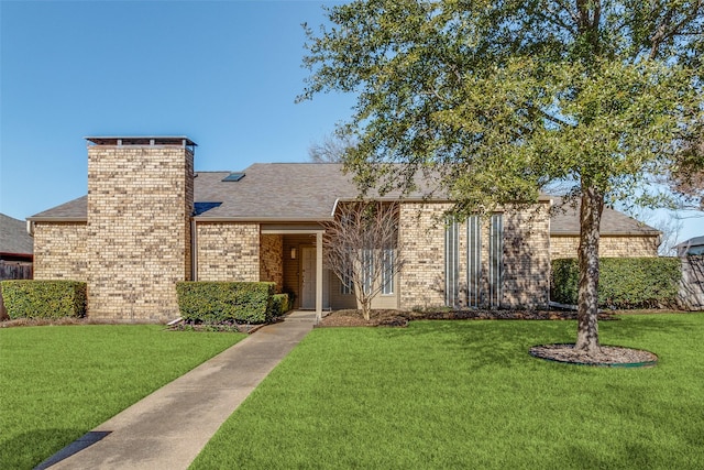 view of front of property with a front yard, brick siding, a chimney, and roof with shingles