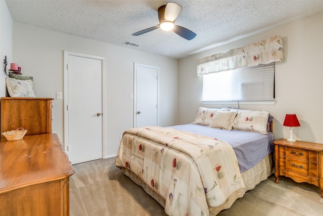 bedroom with ceiling fan, visible vents, a textured ceiling, and light colored carpet