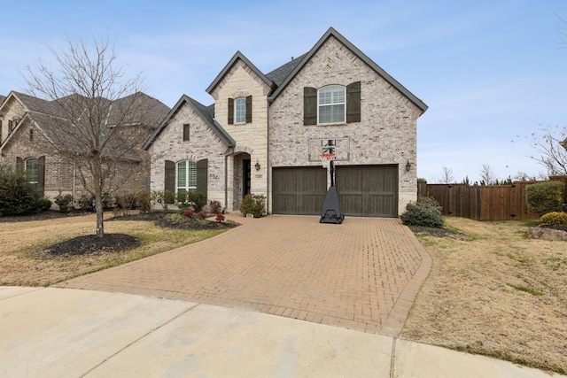 french country style house with an attached garage, fence, decorative driveway, and brick siding