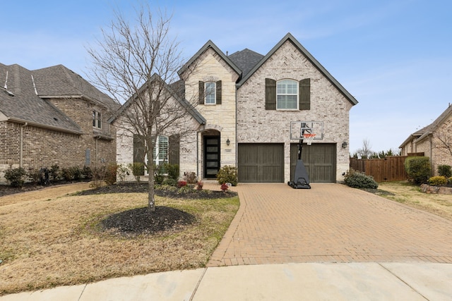 french provincial home featuring an attached garage, brick siding, fence, stone siding, and decorative driveway