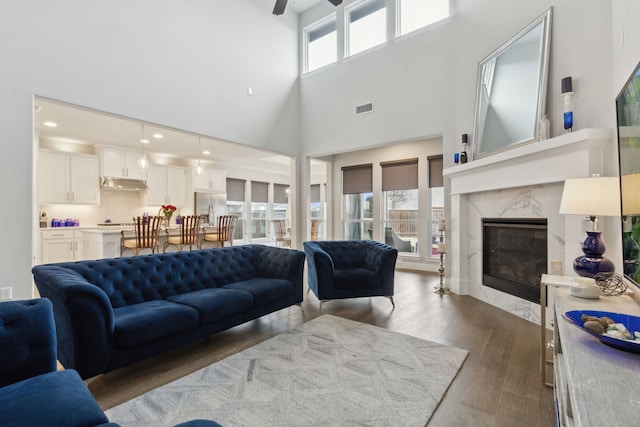 1600 Pebblebrook Ln, Prosper, TX 75078 - living area with visible vents, dark wood-style flooring, a ceiling fan, a towering ceiling, and a premium fireplace