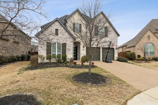 french country home featuring an attached garage, brick siding, fence, decorative driveway, and a front yard