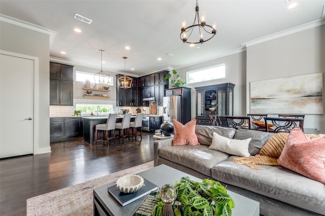 living area with visible vents, dark wood-type flooring, an inviting chandelier, crown molding, and recessed lighting