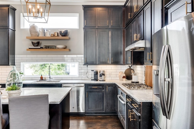 kitchen featuring under cabinet range hood, a sink, appliances with stainless steel finishes, backsplash, and light stone countertops