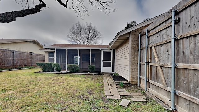 rear view of property featuring a lawn, a fenced backyard, and a sunroom