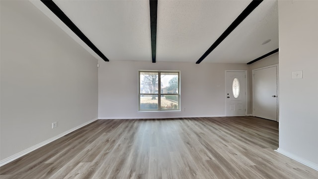 unfurnished living room with light wood-style floors, beamed ceiling, a textured ceiling, and baseboards