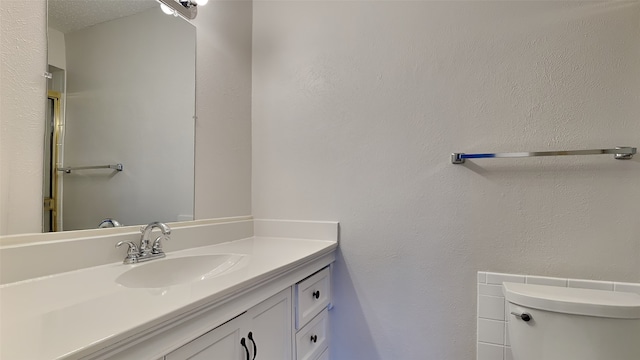 bathroom with a textured wall, vanity, and toilet