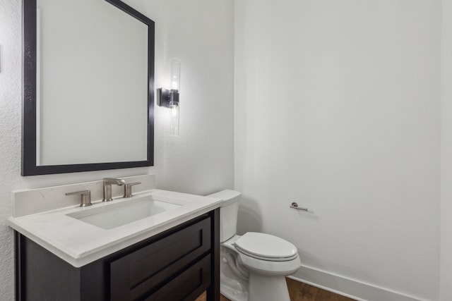 half bath with wood finished floors, vanity, toilet, and baseboards