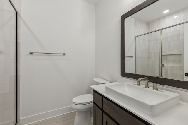 bathroom with vanity, a tile shower, toilet, and baseboards