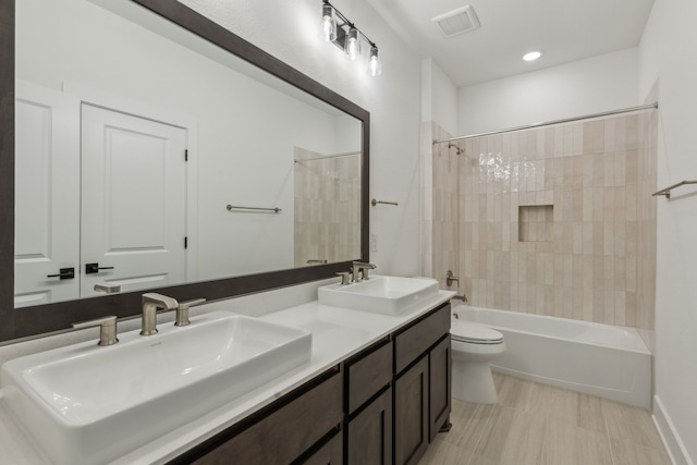 bathroom featuring toilet, double vanity, a sink, and shower / bathtub combination