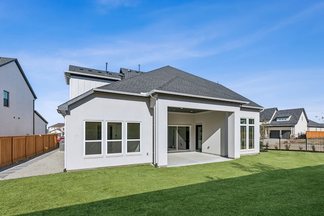 rear view of property featuring a patio, a shingled roof, a lawn, and a fenced backyard