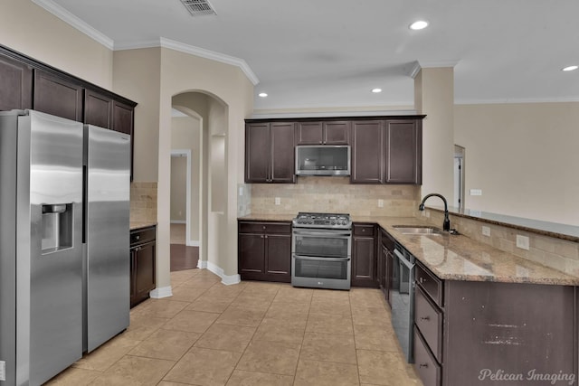 kitchen with appliances with stainless steel finishes, a sink, dark brown cabinetry, light stone countertops, and a peninsula