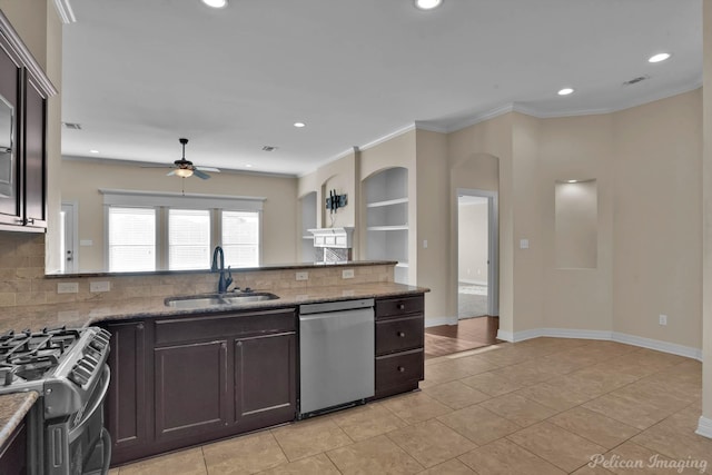 kitchen featuring dark brown cabinetry, decorative backsplash, stainless steel appliances, crown molding, and a sink