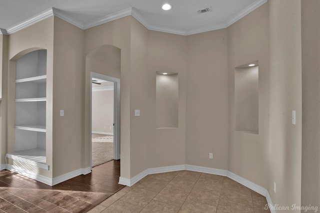 spare room with wood finished floors, visible vents, baseboards, built in features, and ornamental molding