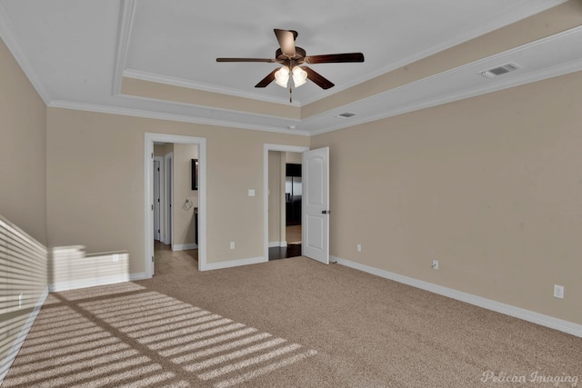 interior space with carpet, a tray ceiling, crown molding, visible vents, and baseboards