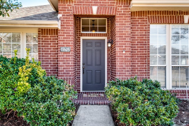 view of exterior entry featuring a shingled roof and brick siding