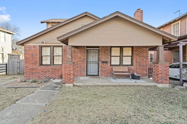 bungalow with a chimney, fence, and brick siding