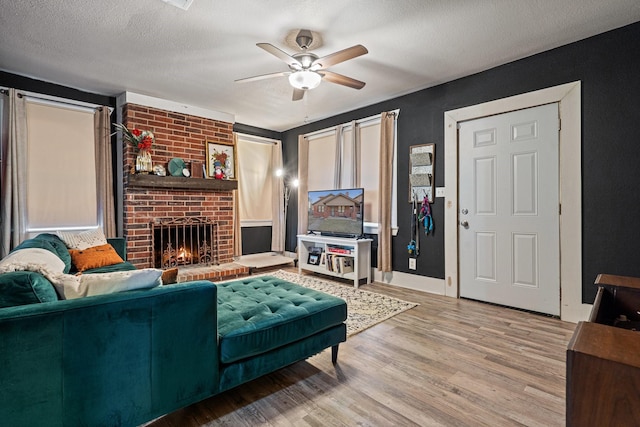 living room featuring baseboards, a ceiling fan, wood finished floors, a textured ceiling, and a fireplace