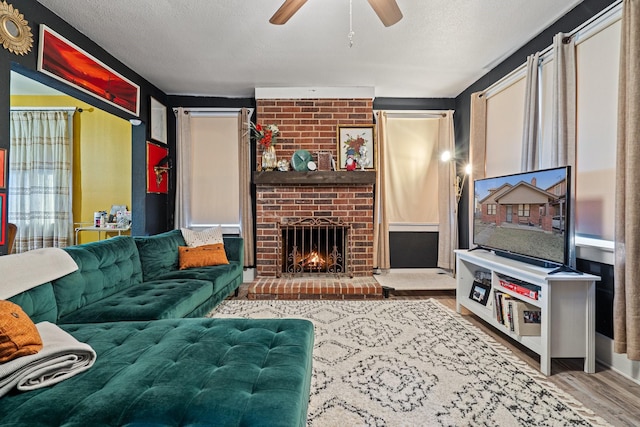 living area featuring a textured ceiling, ceiling fan, a fireplace, and wood finished floors