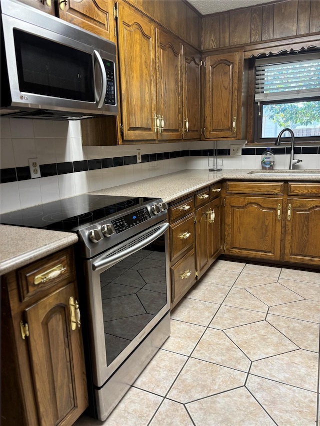 kitchen featuring stainless steel appliances, light countertops, decorative backsplash, light tile patterned flooring, and a sink