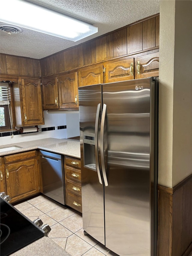 kitchen with a textured ceiling, appliances with stainless steel finishes, light tile patterned flooring, and a sink