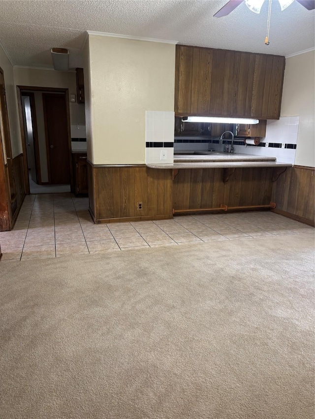 kitchen with wooden walls, light colored carpet, wainscoting, ornamental molding, and a textured ceiling