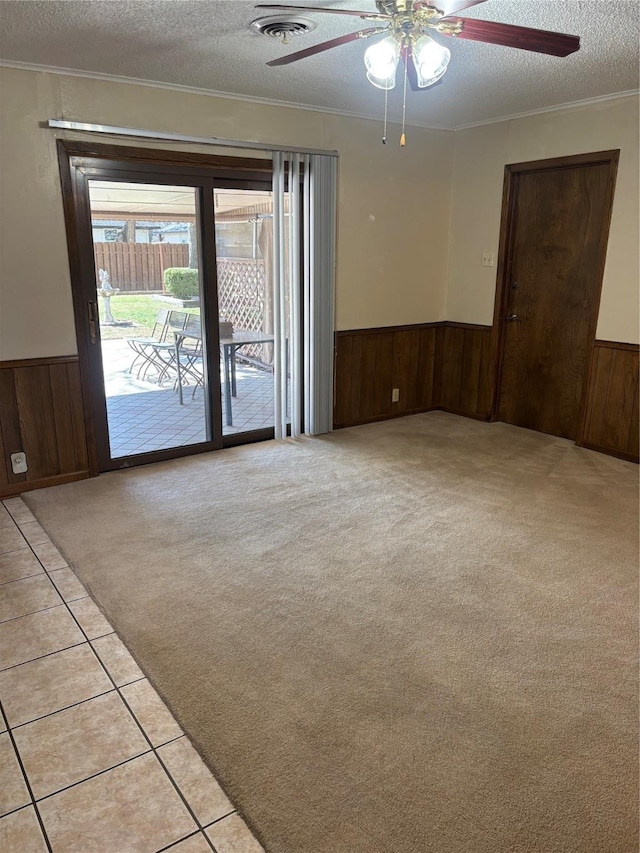 spare room with a textured ceiling, wainscoting, visible vents, and light colored carpet