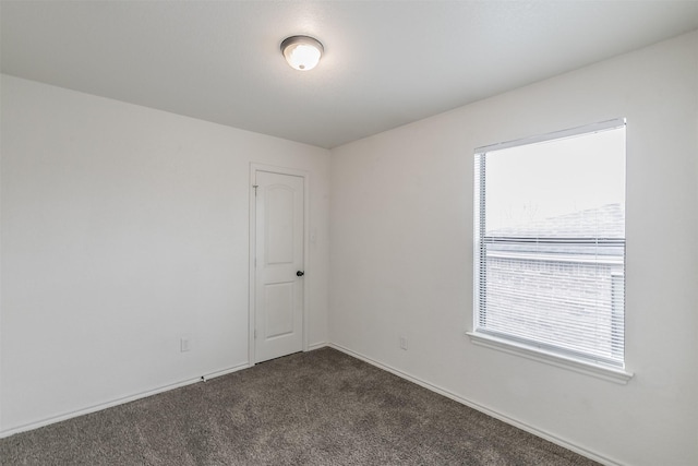 spare room featuring dark carpet and baseboards