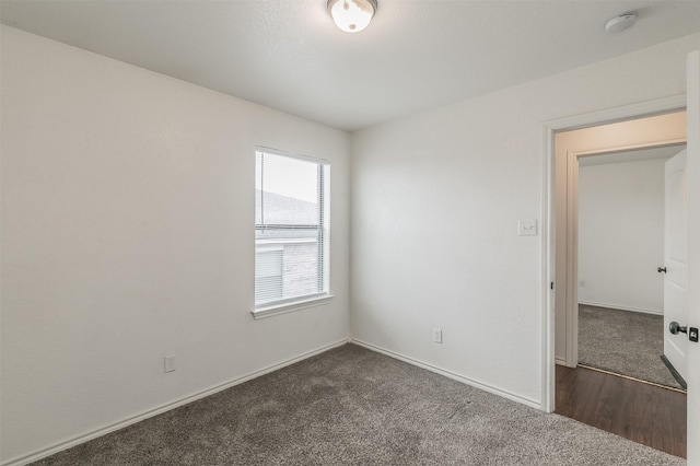 unfurnished room with dark colored carpet and baseboards