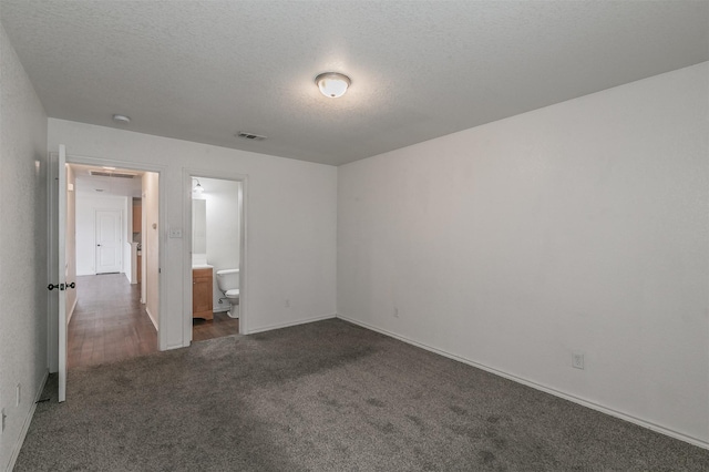 unfurnished bedroom with baseboards, visible vents, ensuite bathroom, dark colored carpet, and a textured ceiling