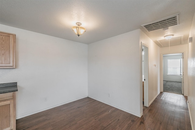 unfurnished room featuring dark wood-style floors, attic access, visible vents, and baseboards